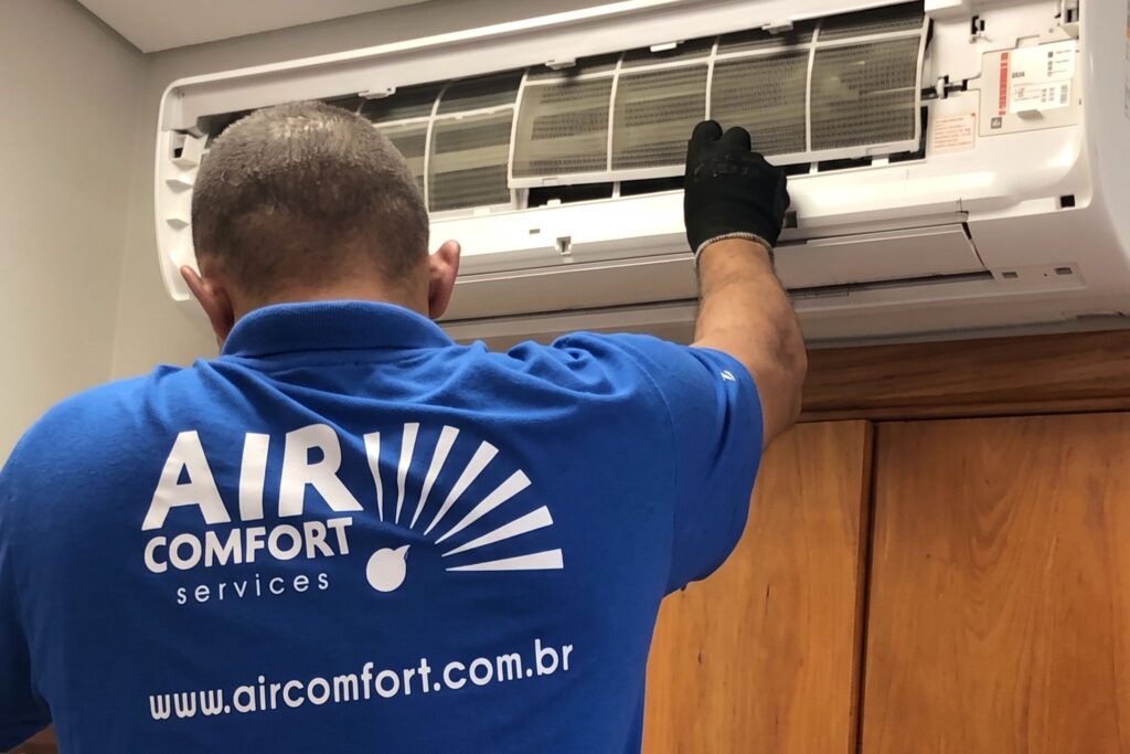 Técnico da AirComfort de uniforme azul abrindo um ar condicionado split para a manutenção